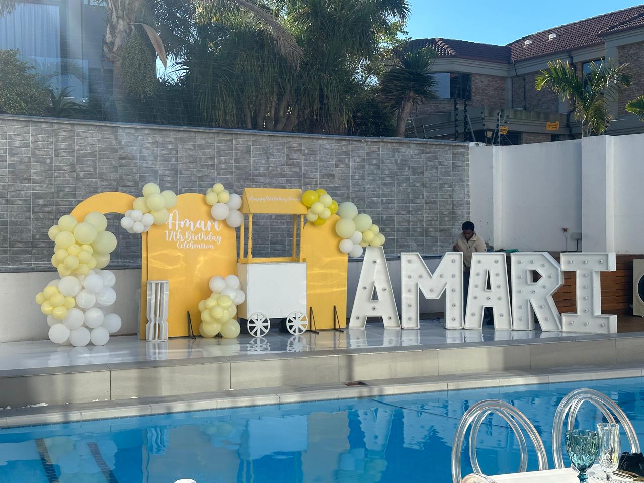Yellow birthday backdrop with balloon garland, treat cart and marquee name letters