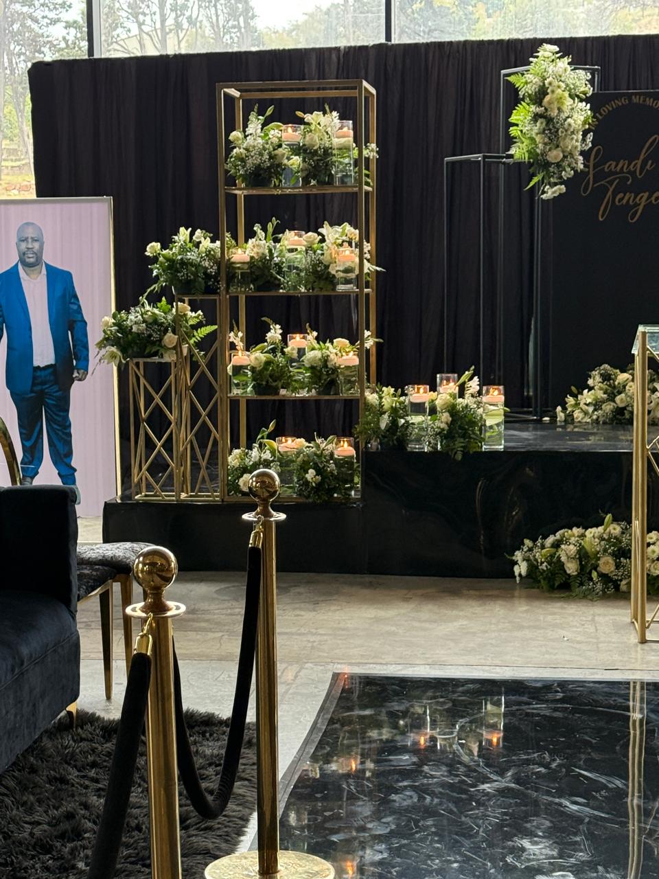 Memorial setup with black draping, gold shelving, white florals and candles