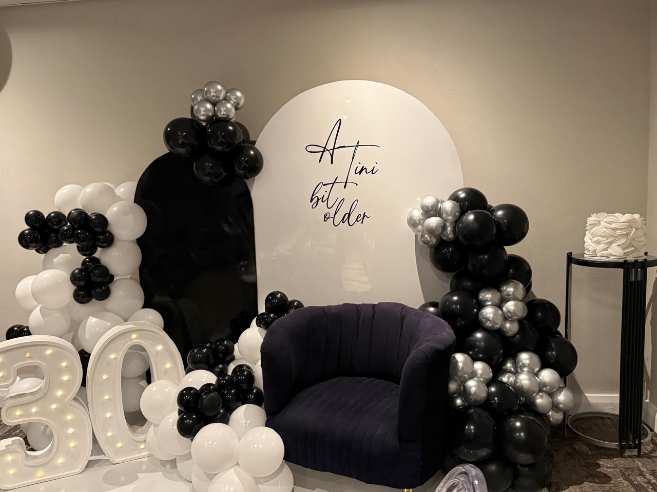 'A Tini Bit Older' arch backdrop with black and silver balloons