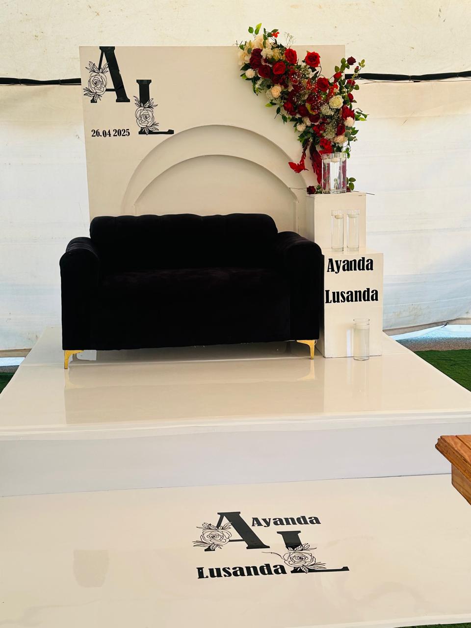 White arch monogram backdrop with red and white florals and black velvet couch