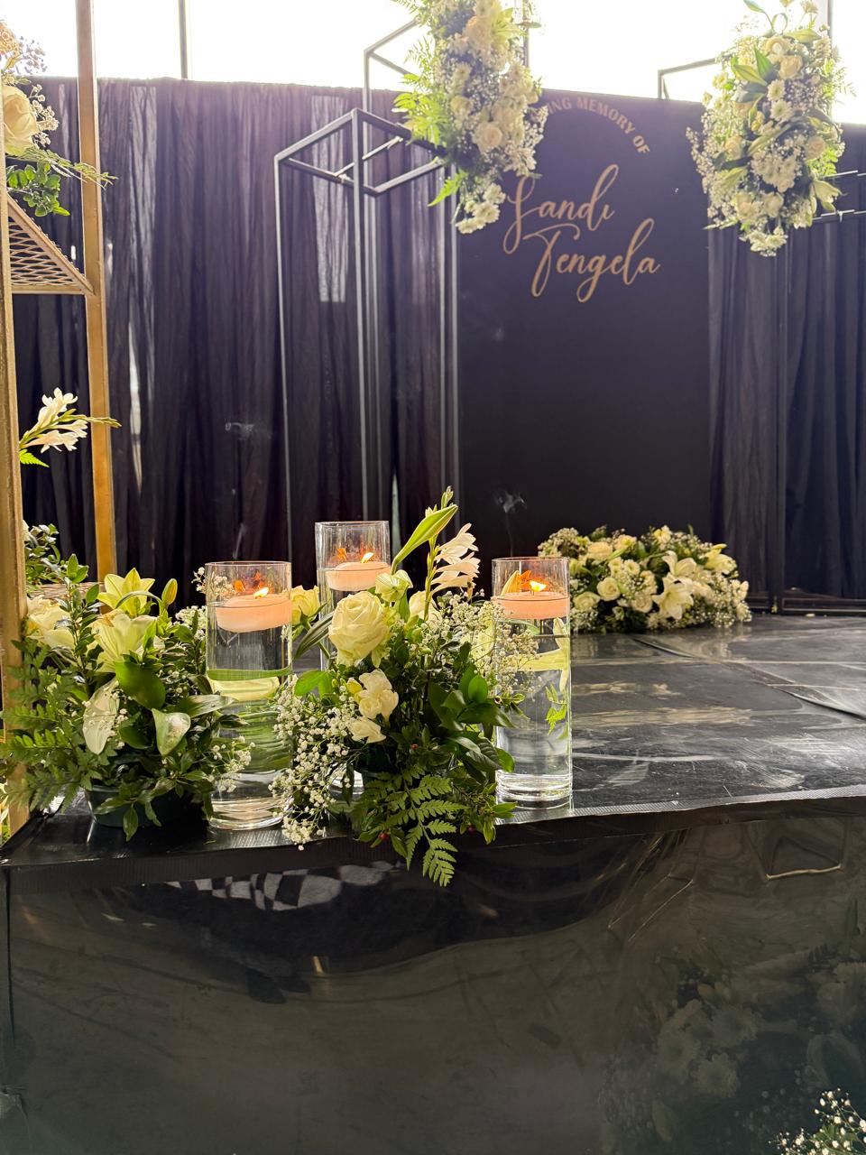 Memorial stage edge with floating candles and white rose arrangements